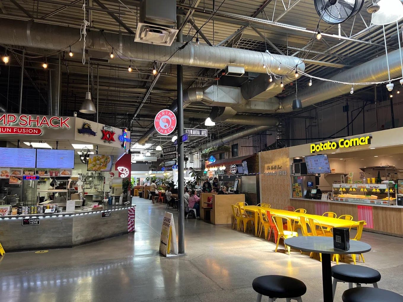 Inside Haven City Market, food stalls under exposed ductwork and string lights with yellow chairs at communal tables