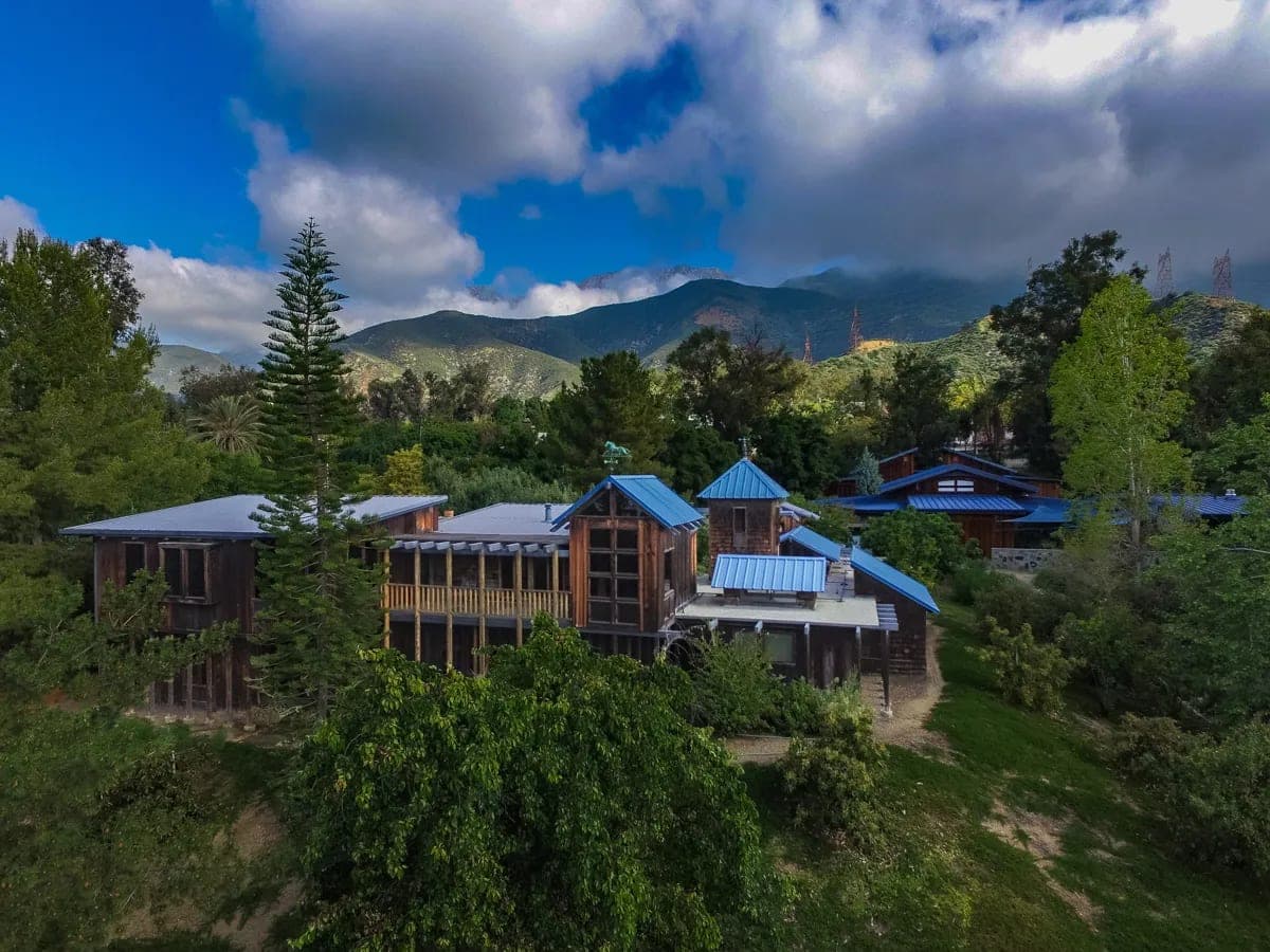 The Maloof compound from above, dark timber buildings with blue metal roofs set among trees below the San Gabriel foothills